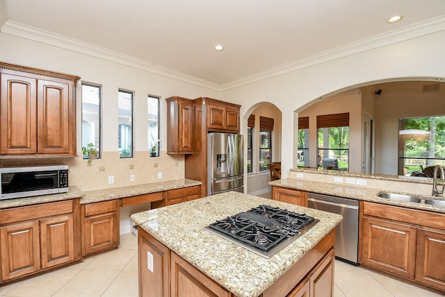 kitchen featuring light stone counters, ornamental molding, sink, a kitchen island, and stainless steel appliances