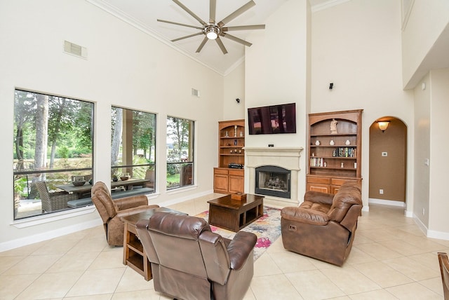 tiled living room featuring a premium fireplace, a towering ceiling, crown molding, ceiling fan, and built in features