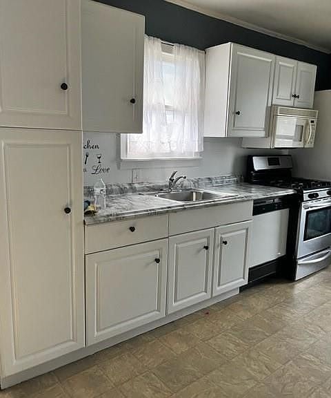 kitchen featuring appliances with stainless steel finishes, white cabinets, light tile patterned floors, and sink