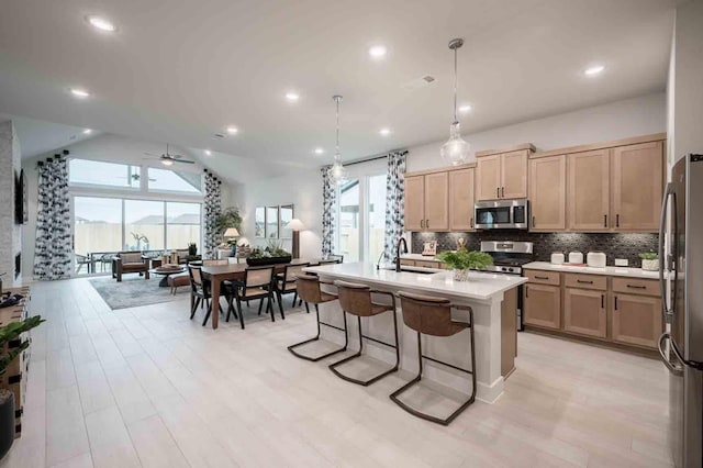 kitchen featuring a kitchen breakfast bar, ceiling fan, pendant lighting, a kitchen island with sink, and appliances with stainless steel finishes