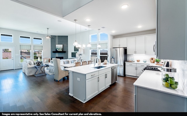 kitchen with dark hardwood / wood-style floors, a center island with sink, appliances with stainless steel finishes, a fireplace, and ceiling fan