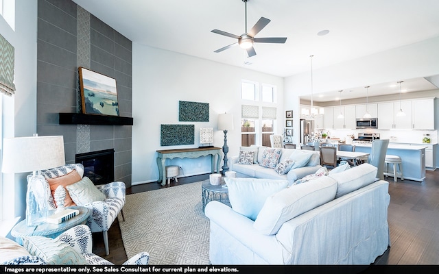 living room with a towering ceiling, a tiled fireplace, ceiling fan, and dark hardwood / wood-style flooring