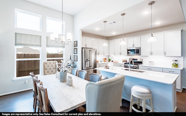 kitchen featuring decorative light fixtures, white cabinets, stainless steel appliances, and a center island with sink