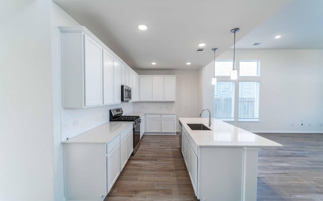 kitchen featuring decorative light fixtures, white cabinetry, sink, a kitchen island with sink, and stainless steel appliances