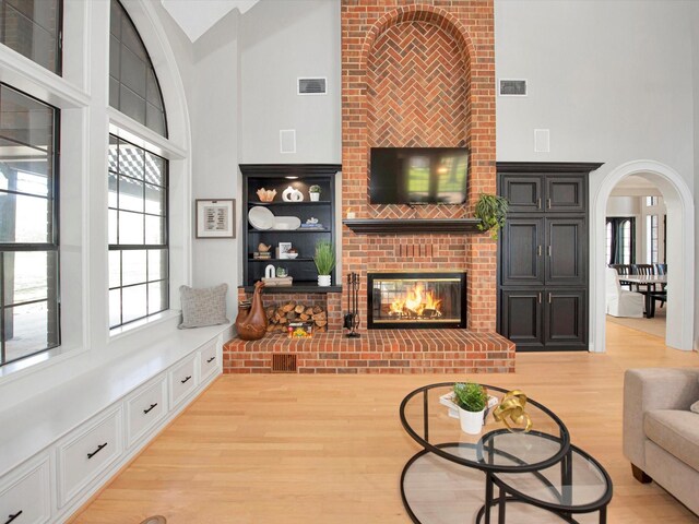 living room with brick wall, a high ceiling, light hardwood / wood-style flooring, and a brick fireplace