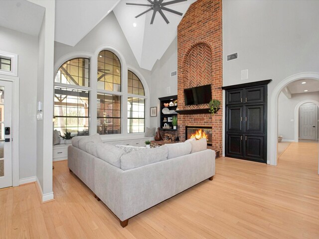 living room featuring high vaulted ceiling, a fireplace, light wood-type flooring, ceiling fan, and brick wall