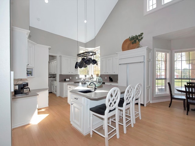 kitchen with light hardwood / wood-style floors, high vaulted ceiling, tasteful backsplash, and white cabinets