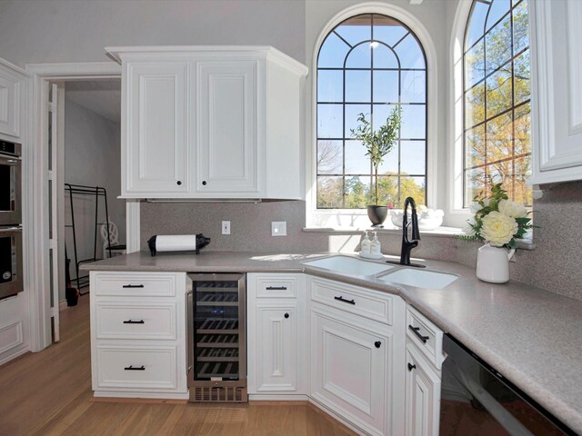 kitchen with light hardwood / wood-style flooring, dishwasher, tasteful backsplash, sink, and wine cooler