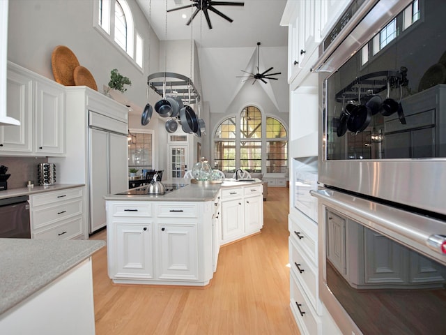 kitchen with light hardwood / wood-style flooring, a high ceiling, white cabinets, a center island, and ceiling fan