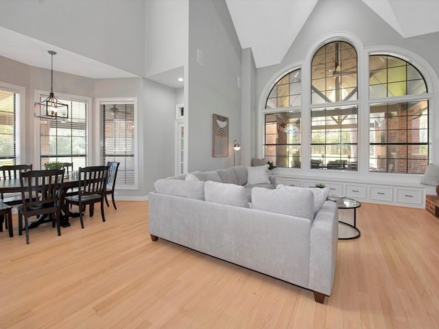 living room featuring high vaulted ceiling, an inviting chandelier, and light hardwood / wood-style floors