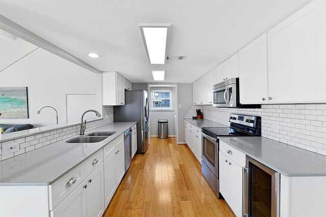 kitchen with sink, appliances with stainless steel finishes, wine cooler, light hardwood / wood-style floors, and white cabinetry