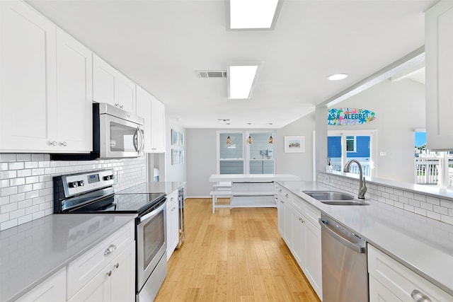 kitchen with sink, appliances with stainless steel finishes, light hardwood / wood-style floors, tasteful backsplash, and white cabinetry