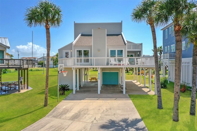 coastal home with an attached garage, concrete driveway, a front lawn, and a shingled roof