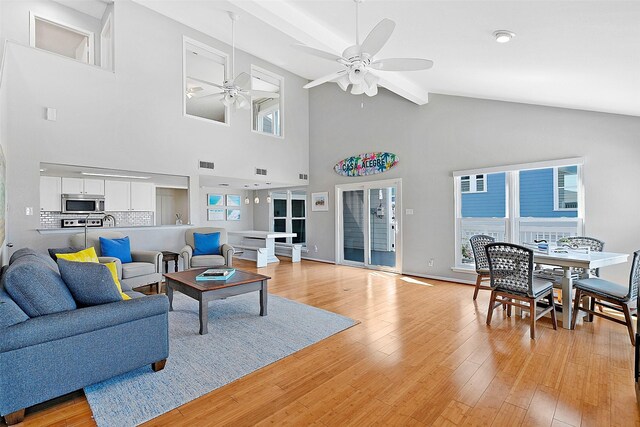 living room with ceiling fan, high vaulted ceiling, light hardwood / wood-style floors, and beam ceiling