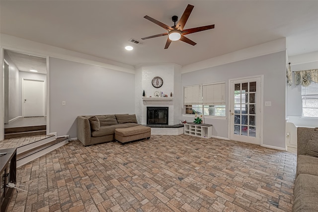 living room featuring ceiling fan, brick wall, a brick fireplace, and a healthy amount of sunlight