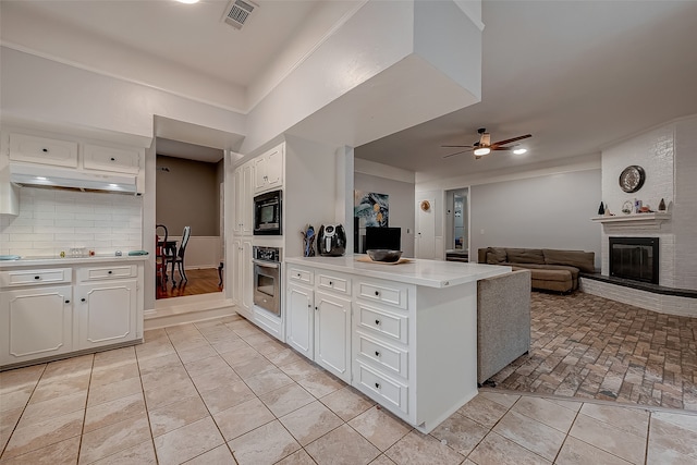 kitchen featuring ceiling fan, backsplash, black microwave, stainless steel oven, and a fireplace