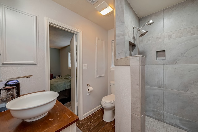 bathroom with toilet, a tile shower, and vanity