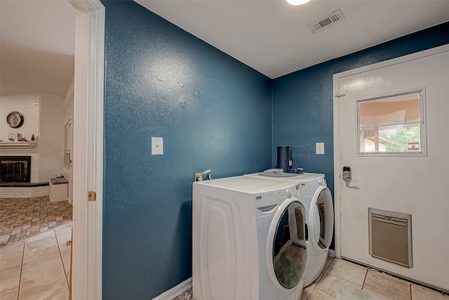 clothes washing area with independent washer and dryer, a brick fireplace, and light tile patterned flooring