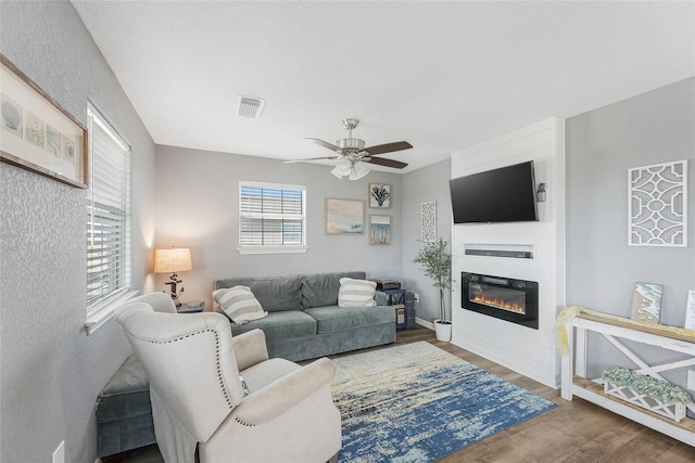 living area featuring a glass covered fireplace, visible vents, ceiling fan, and wood finished floors