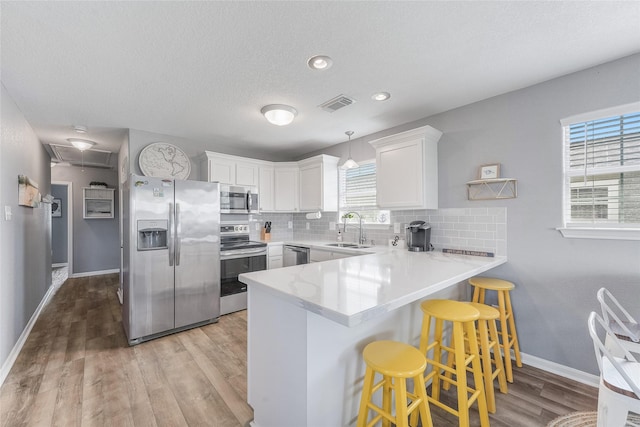 kitchen with a peninsula, a sink, white cabinetry, appliances with stainless steel finishes, and tasteful backsplash