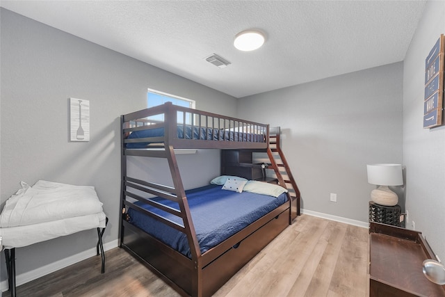 bedroom with a textured ceiling, wood finished floors, visible vents, and baseboards