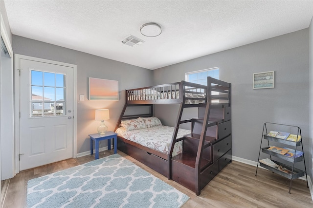 bedroom featuring visible vents, a textured ceiling, baseboards, and wood finished floors