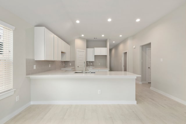 kitchen with light hardwood / wood-style floors, white cabinetry, sink, and kitchen peninsula