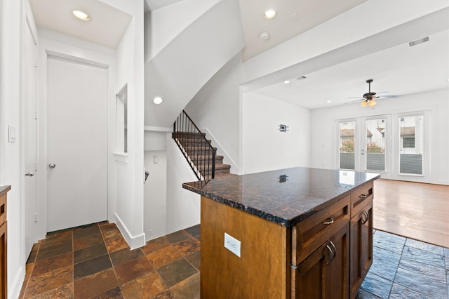 kitchen with ceiling fan, dark stone counters, dark wood-type flooring, and a kitchen island