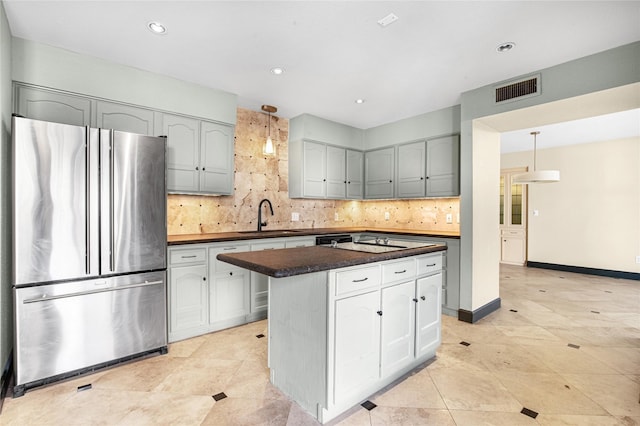 kitchen featuring stainless steel fridge, backsplash, sink, a kitchen island, and hanging light fixtures