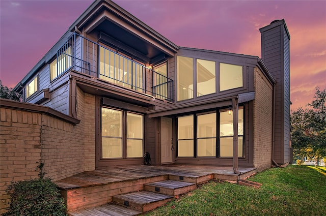 back house at dusk featuring a yard and a balcony