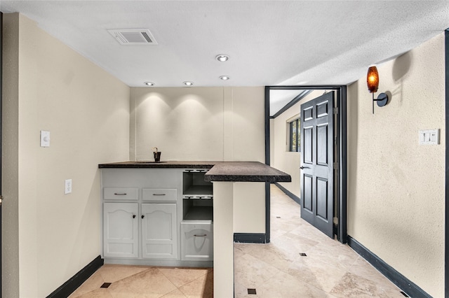 kitchen featuring kitchen peninsula, sink, light tile patterned flooring, and a textured ceiling