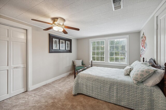 bedroom with ceiling fan, ornamental molding, a closet, and carpet floors