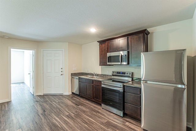 kitchen featuring sink, dark stone counters, dark wood-type flooring, and stainless steel appliances