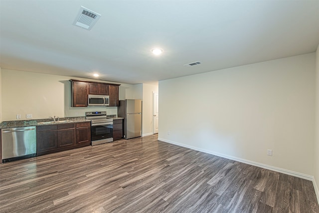 kitchen with dark brown cabinetry, hardwood / wood-style flooring, stone counters, sink, and stainless steel appliances