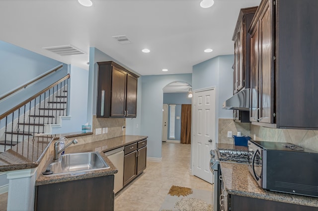 kitchen featuring decorative backsplash, stainless steel appliances, dark stone counters, sink, and dark brown cabinetry