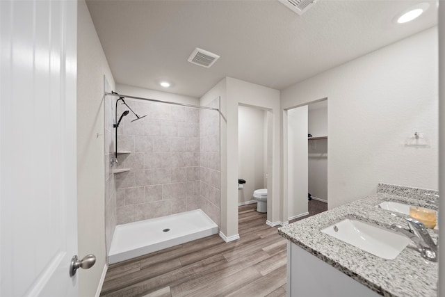 bathroom featuring wood-type flooring, toilet, a tile shower, and vanity