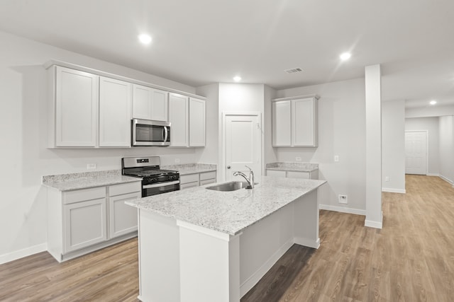 kitchen featuring sink, white cabinets, light stone counters, an island with sink, and stainless steel appliances