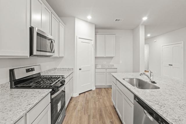 kitchen featuring light stone countertops, white cabinets, stainless steel appliances, light hardwood / wood-style floors, and sink