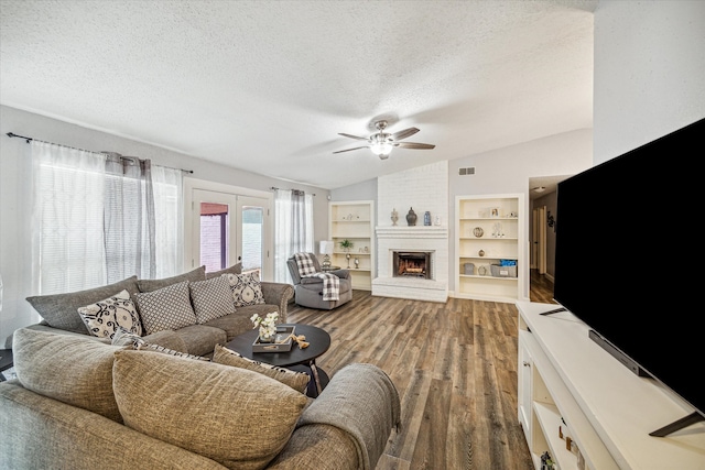 living room featuring ceiling fan, a brick fireplace, wood-type flooring, a textured ceiling, and lofted ceiling