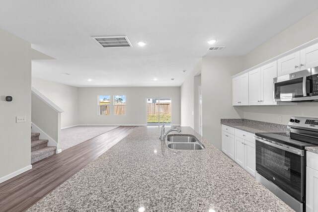 kitchen with hardwood / wood-style floors, light stone counters, appliances with stainless steel finishes, white cabinetry, and sink