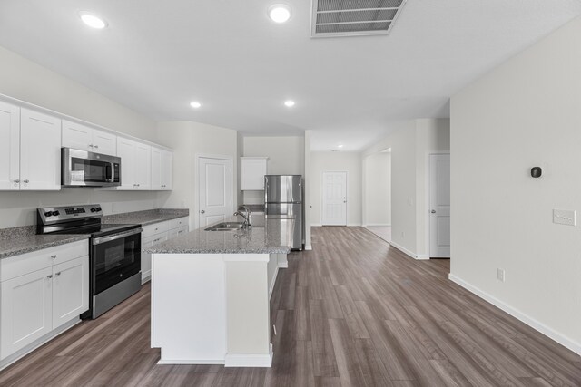 kitchen with light stone countertops, hardwood / wood-style floors, stainless steel appliances, white cabinets, and a center island with sink