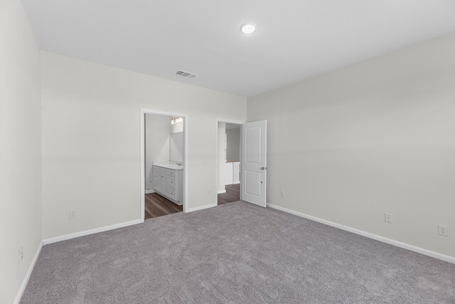 unfurnished bedroom with connected bathroom and dark colored carpet