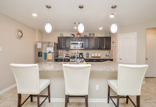 kitchen featuring appliances with stainless steel finishes, backsplash, an island with sink, and a breakfast bar