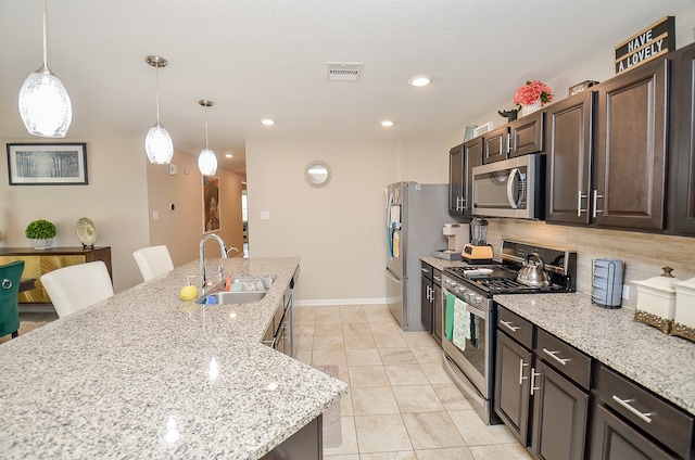 kitchen with a breakfast bar, sink, appliances with stainless steel finishes, dark brown cabinetry, and light stone countertops