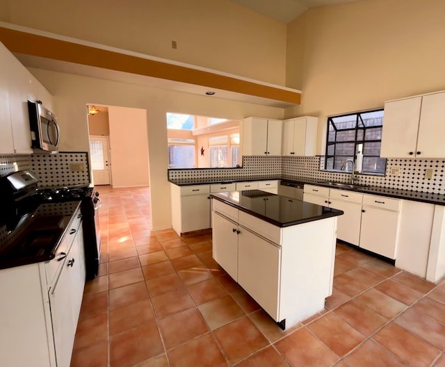 kitchen featuring stainless steel appliances, a center island, light tile patterned floors, backsplash, and white cabinetry