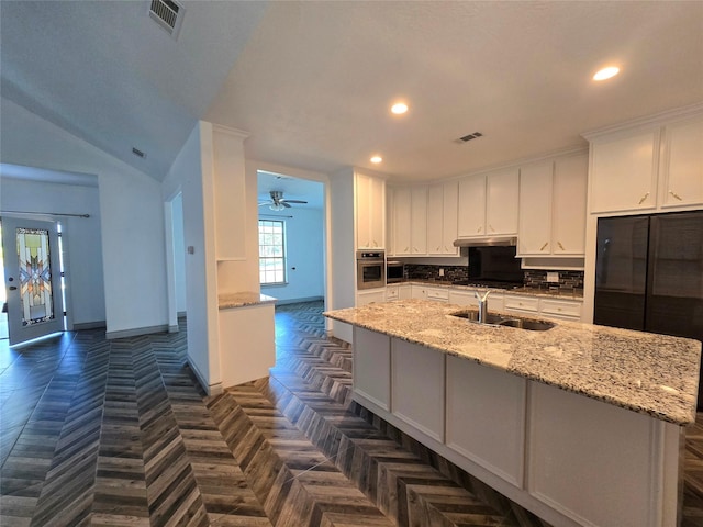 kitchen featuring light stone counters, oven, sink, and white cabinets