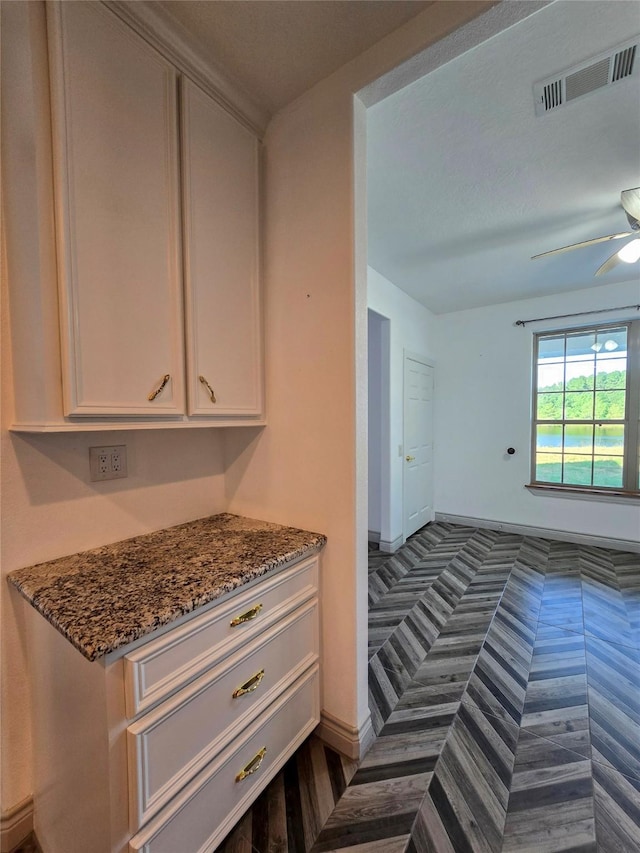 kitchen featuring ceiling fan, dark stone counters, and white cabinets