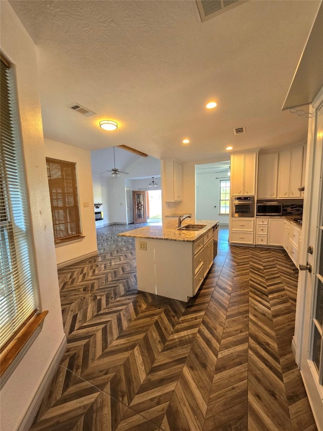 kitchen with sink, white cabinetry, light stone counters, stainless steel appliances, and a kitchen island with sink