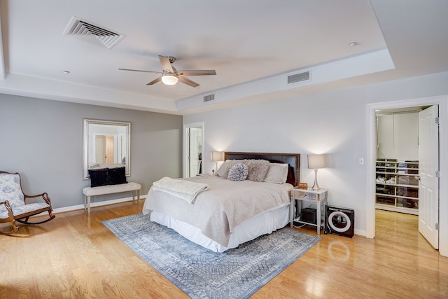 bedroom featuring a tray ceiling, a spacious closet, ceiling fan, and light hardwood / wood-style flooring