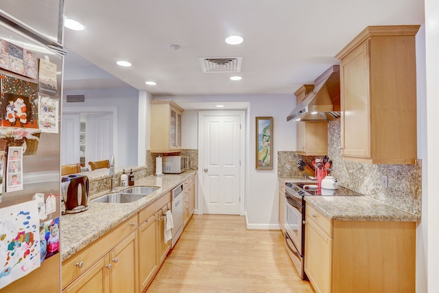 kitchen with light brown cabinetry, appliances with stainless steel finishes, wall chimney exhaust hood, and light hardwood / wood-style flooring